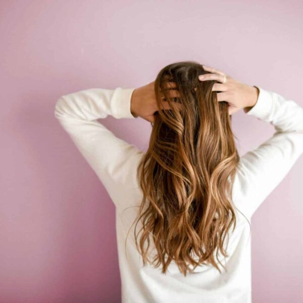 Back view of a woman with elegant long brown hair against a pink wall, showcasing stylish hair design. hair masks