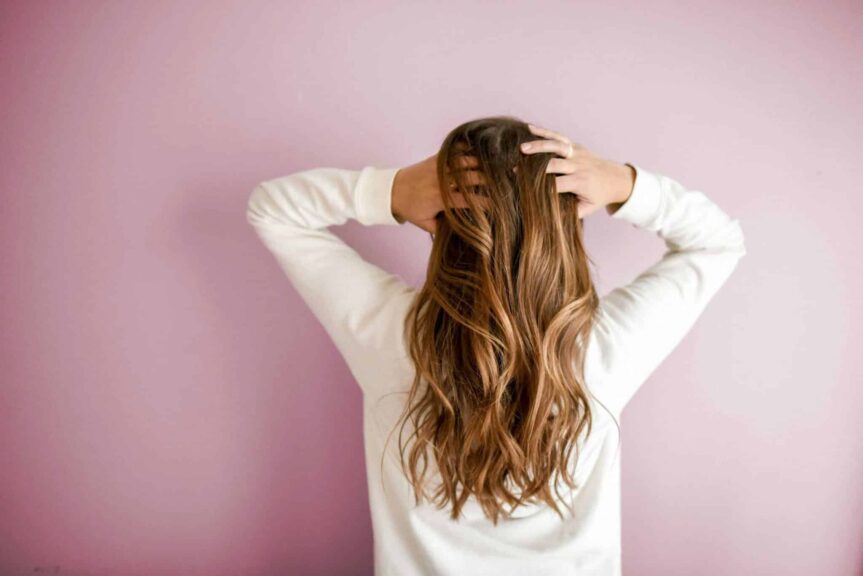 Back view of a woman with elegant long brown hair against a pink wall, showcasing stylish hair design. hair masks