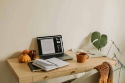 This photograph has a desk, a laptop, and notebooks. Fall dorm decor can provide a cozy studying atmosphere.