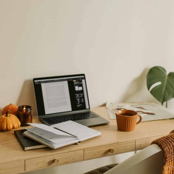 This photograph has a desk, a laptop, and notebooks. Fall dorm decor can provide a cozy studying atmosphere.
