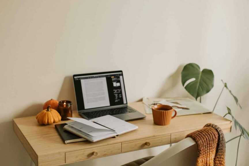 This photograph has a desk, a laptop, and notebooks. Fall dorm decor can provide a cozy studying atmosphere.