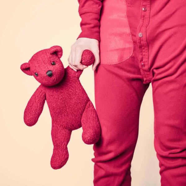 A close-up shot of a person in red pajamas holding a red teddy bear. Inner child, relationships