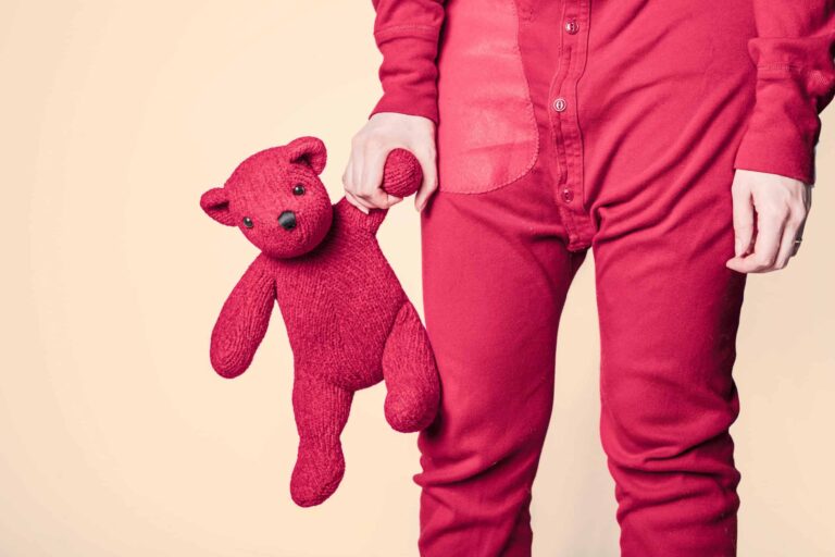 A close-up shot of a person in red pajamas holding a red teddy bear. Inner child, relationships