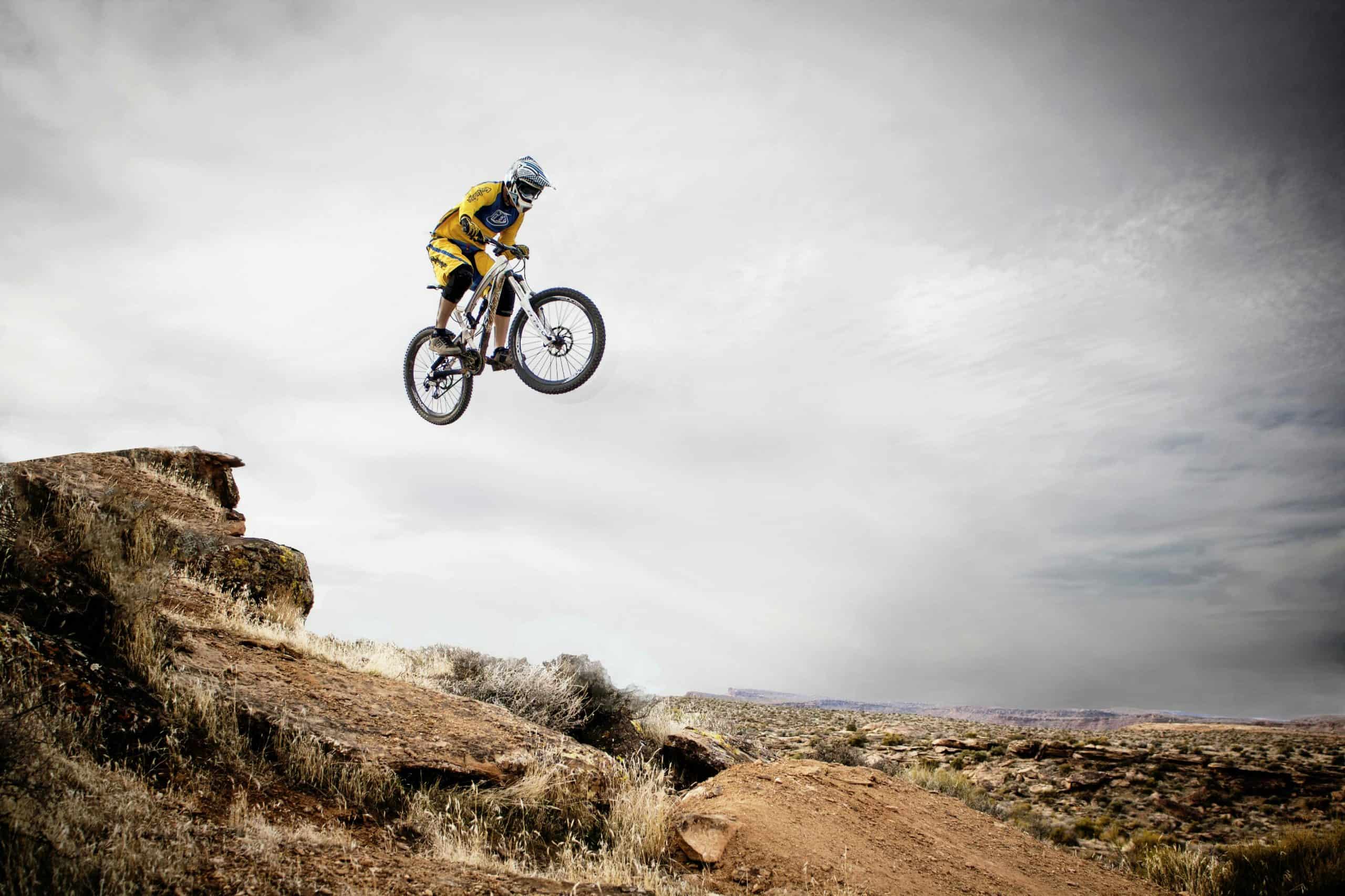 Challenge travel, adventure travel, A cyclist performs a daring jump off a rocky cliff under a cloudy sky.