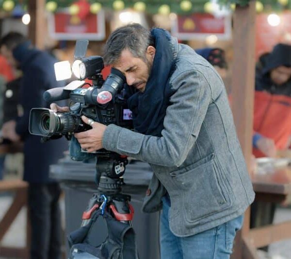 Cameraman recording a movie scene during the SCAD Savannah Film Festival Fest, surrounded by staff, equipment, and evening lights in a winter street photography setting.