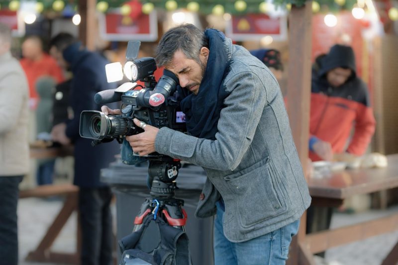 Cameraman recording a movie scene during the SCAD Savannah Film Festival Fest, surrounded by staff, equipment, and evening lights in a winter street photography setting.