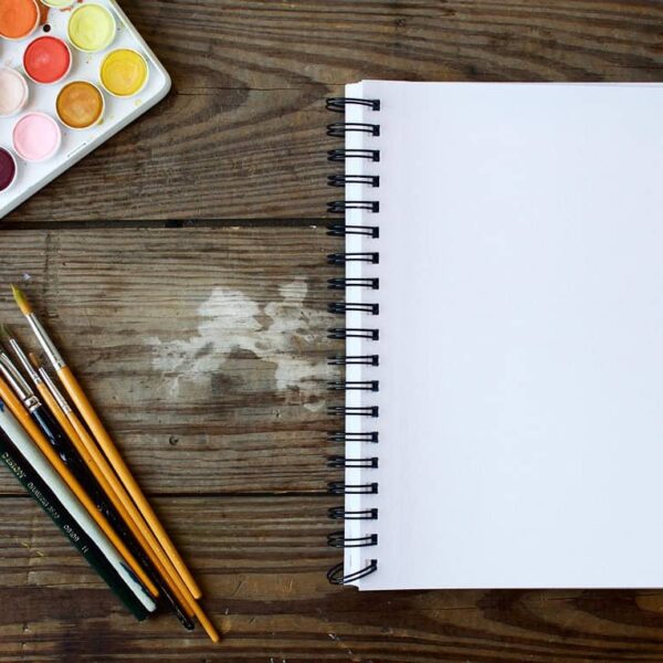 This photograph has a notebook, watercolor paints, and paint brushes. Creativity can be wonderful for brain health.