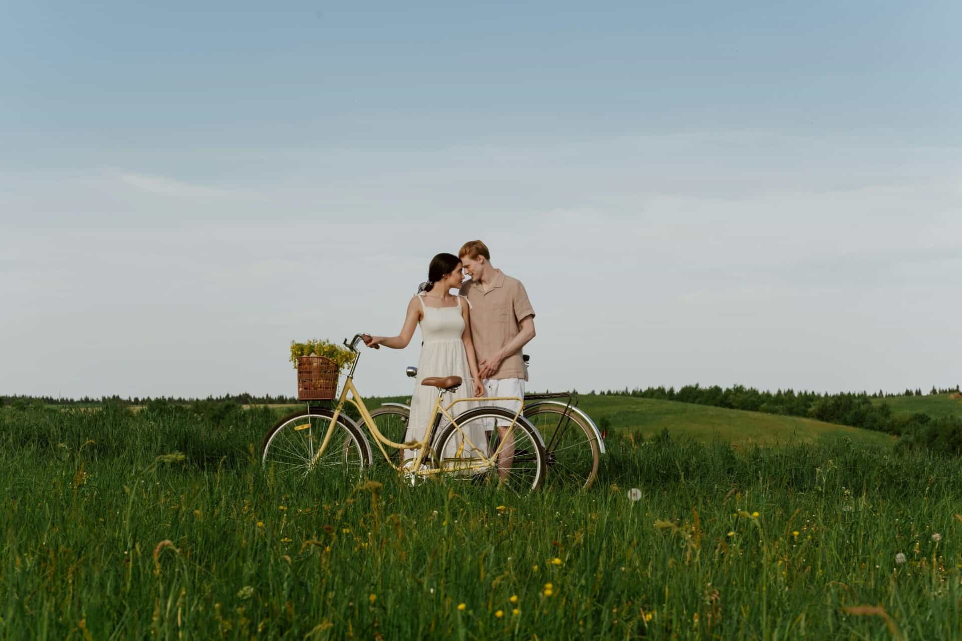 Loving couple with a bike in a grassy summer field, enjoying nature outdoors, healthy relationships