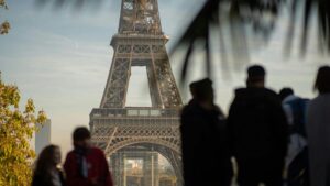 Tourists silhouette in front of Eiffel Tower, Paris landmark in soft daylight.