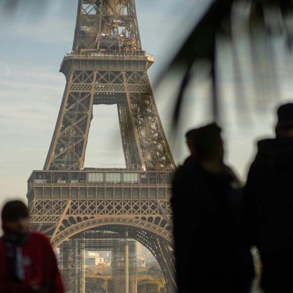 Tourists silhouette in front of Eiffel Tower, Paris landmark in soft daylight.