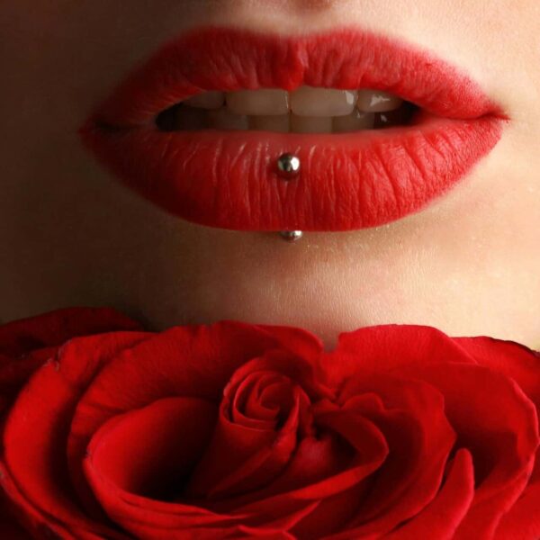 Aesthetic close-up featuring red lipstick, lip piercing, and a red rose. affordable makeup products