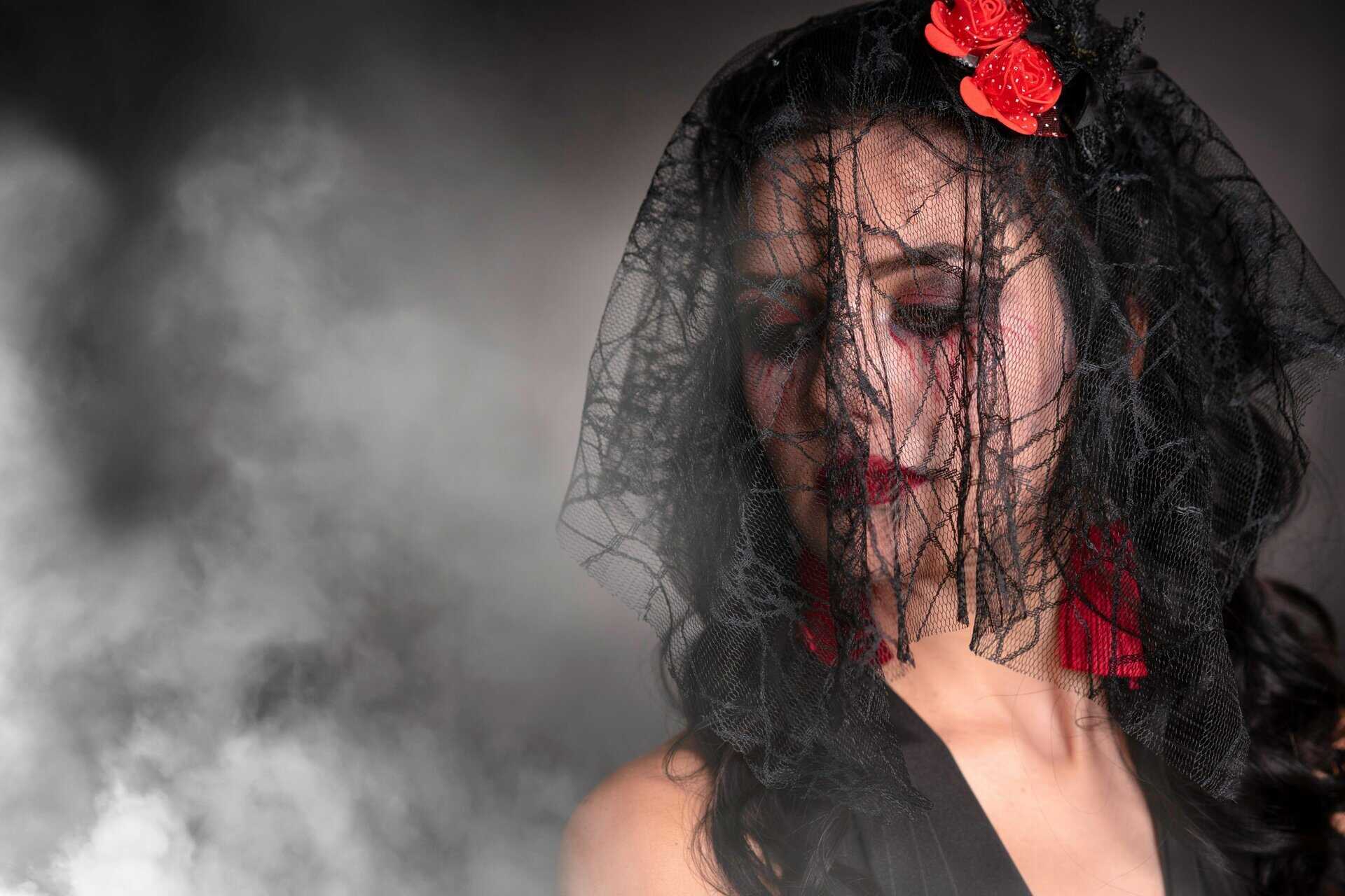 Mysterious woman in black veil with red accessories amidst smoke, evoking a dramatic and elegant mood. Fall fashion, fashion trend