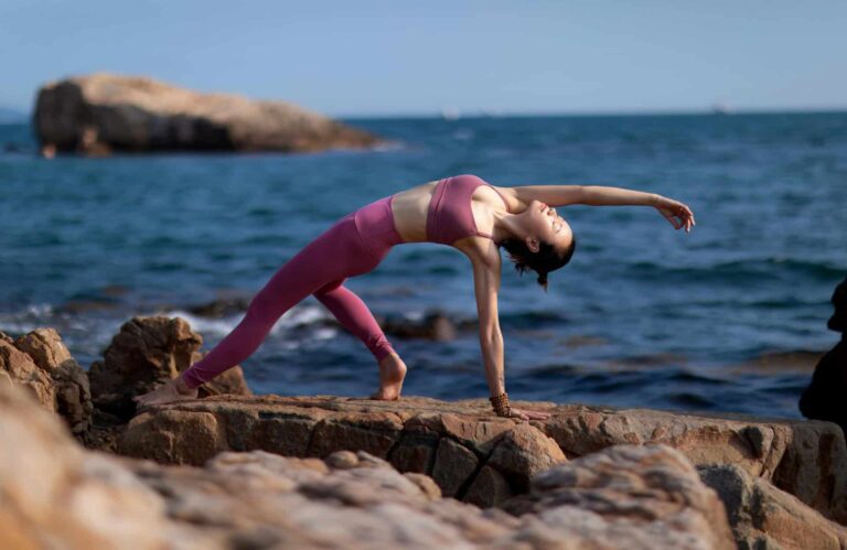 Asian woman practicing yoga on rocky seashore with sea view, showcasing flexibility and strength, wellness, natural immunity