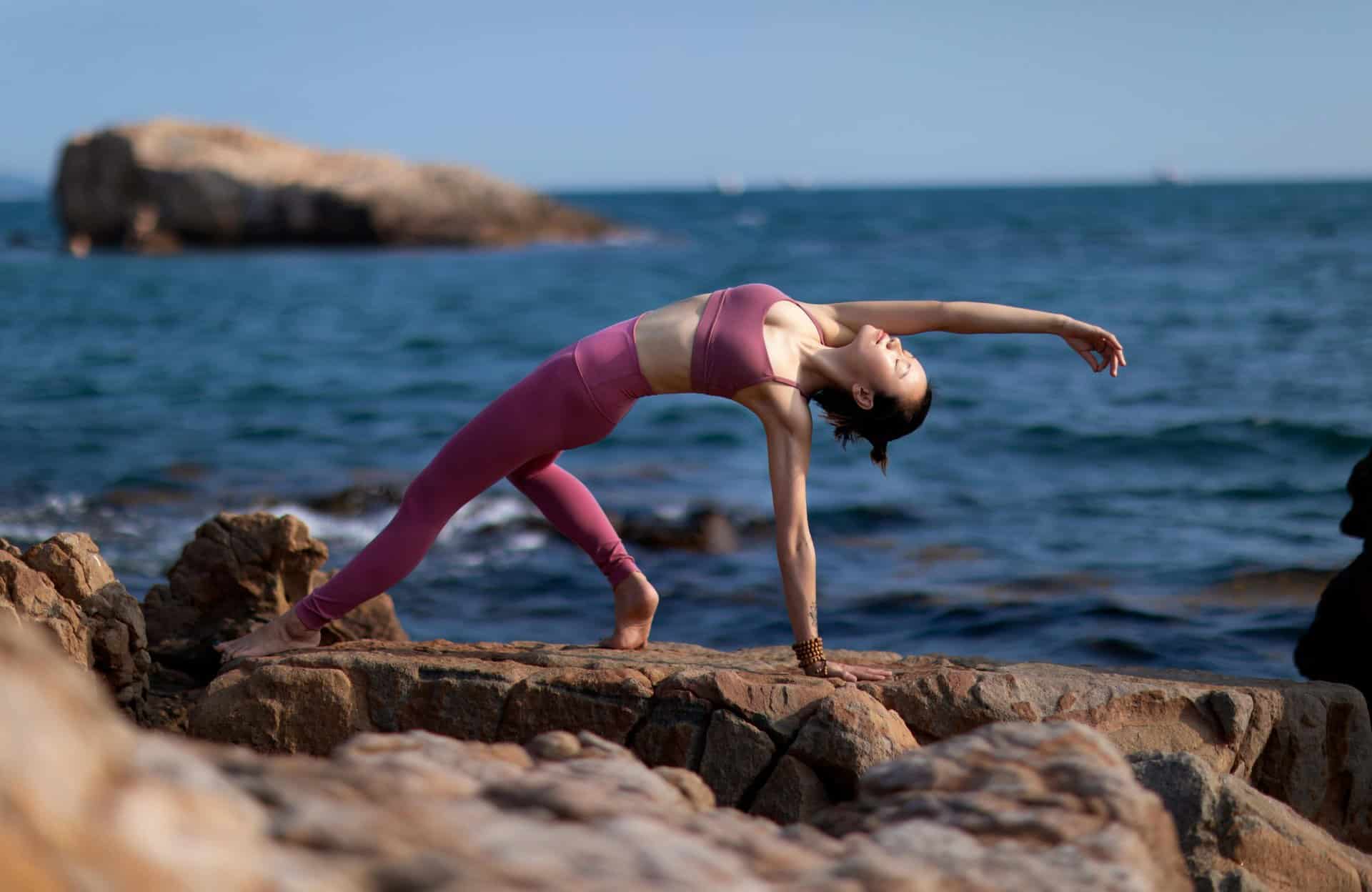 Asian woman practicing yoga on rocky seashore with sea view, showcasing flexibility and strength, wellness, natural immunity