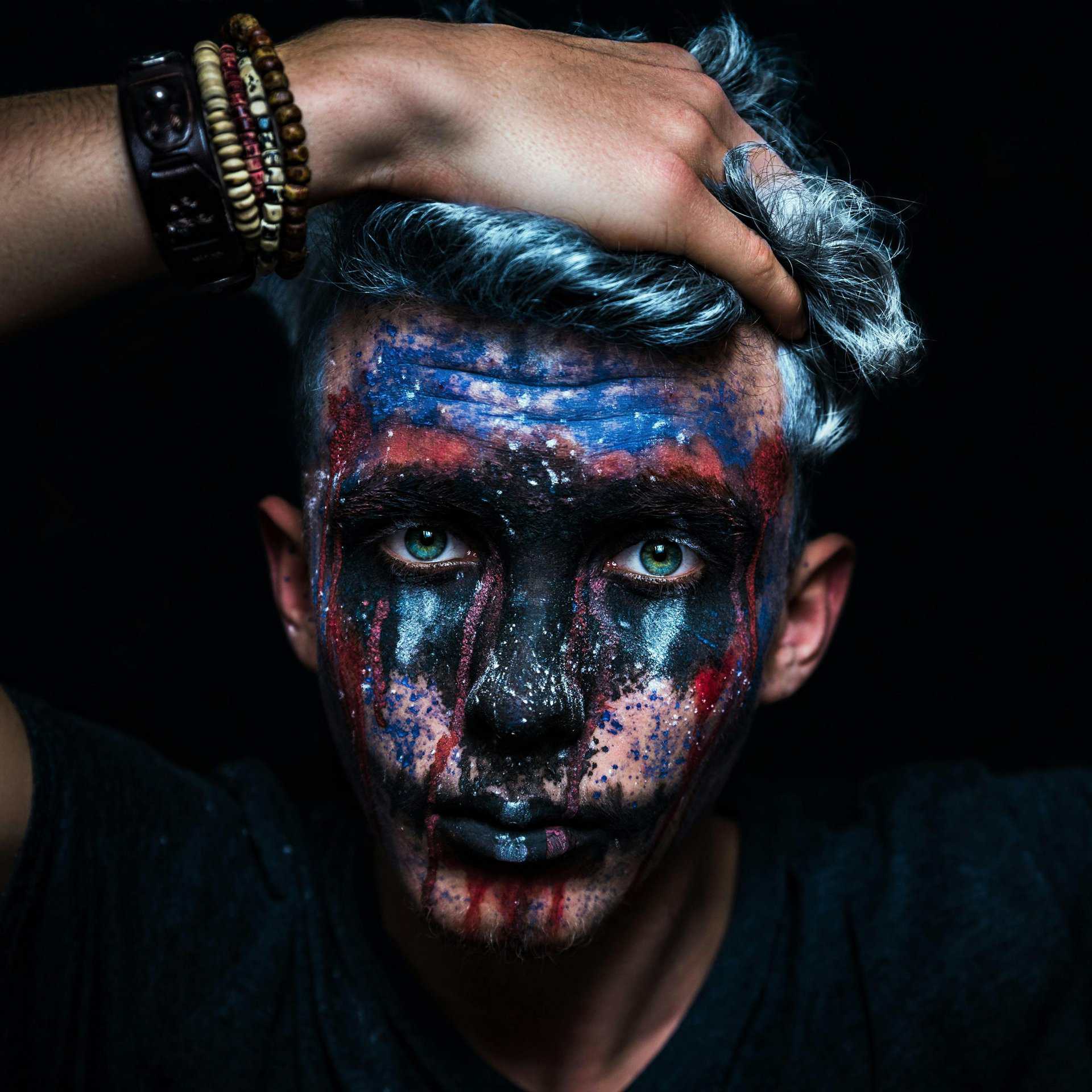 Stunning close-up portrait of a man with vibrant face paint and intense expression, perfect for artistic themes. Protect your skin before putting on Halloween makeup.
