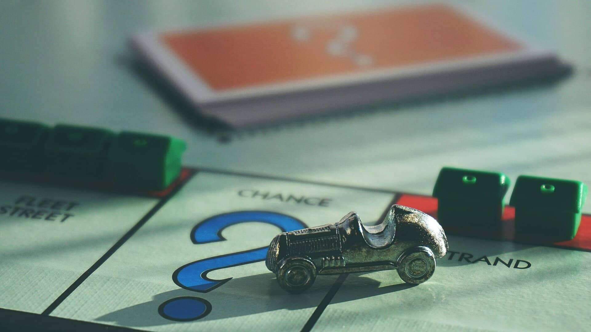 A close-up of a Monopoly board game featuring a silver car token and chance card.