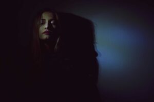 An artistic portrait of a woman with dark and moody lighting creating bold shadows. shadow work