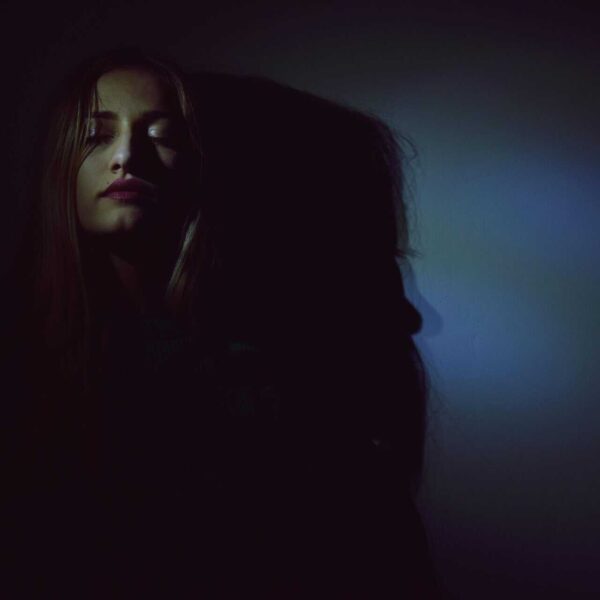 An artistic portrait of a woman with dark and moody lighting creating bold shadows. shadow work