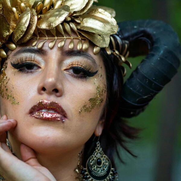 Elegant close-up portrait of a woman in fantasy costume with golden makeup and horns.