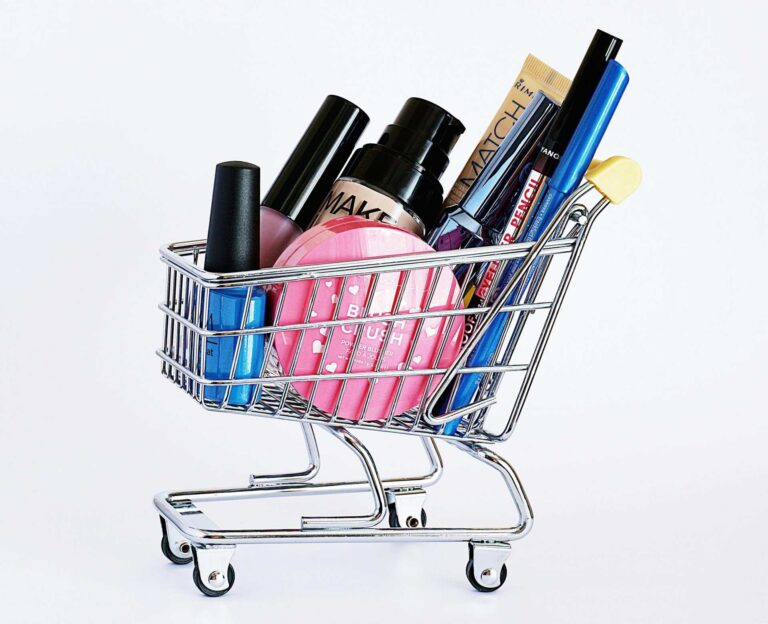 Miniature shopping cart filled with a variety of cosmetics on a white background. beauty releases