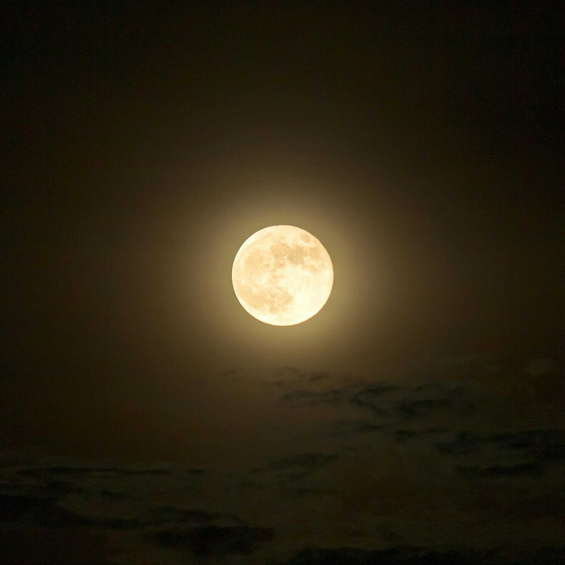 A bright full moon illuminating the night, surrounded by a soft glow against a dark sky.