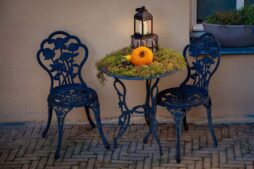 Charming outdoor fall setup with a pumpkin, lantern, and wrought iron furniture.
