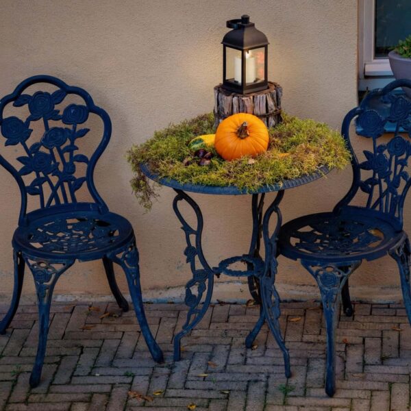 Charming outdoor fall setup with a pumpkin, lantern, and wrought iron furniture.