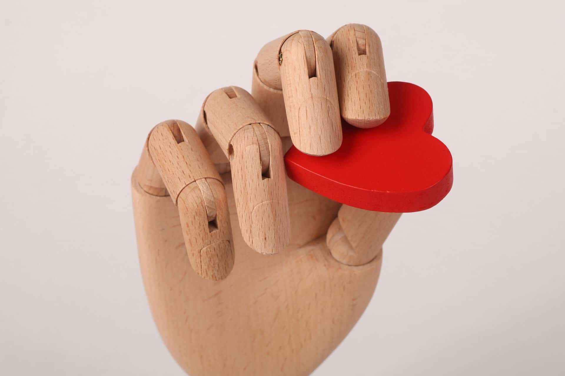 A wooden hand model gripping a red heart symbolizing love and emotion.