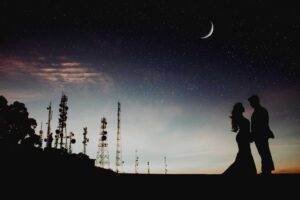 A couple's silhouette against a starry sky with a crescent moon and communication towers, creating a romantic ambiance. love languages, moon sign, astrology,