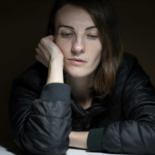 A woman in thought with a serious expression, indoors, in a low-light setting.