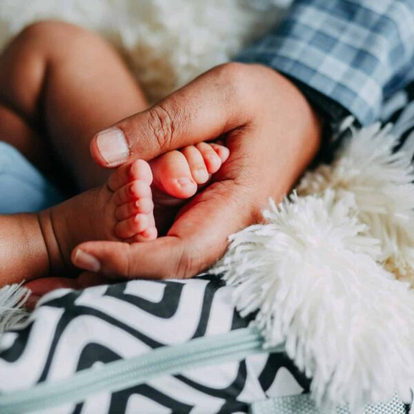 Close-up of an adult hand gently holding a baby's foot, symbolizing care and love. Paternal age, genetic mutation,