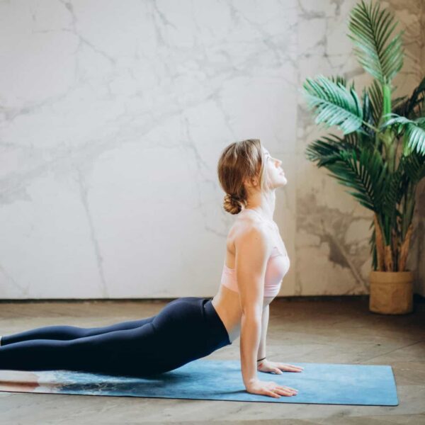Woman in yoga pose on mat, exercising indoors with natural light and plant decor, somatic psychology, healing