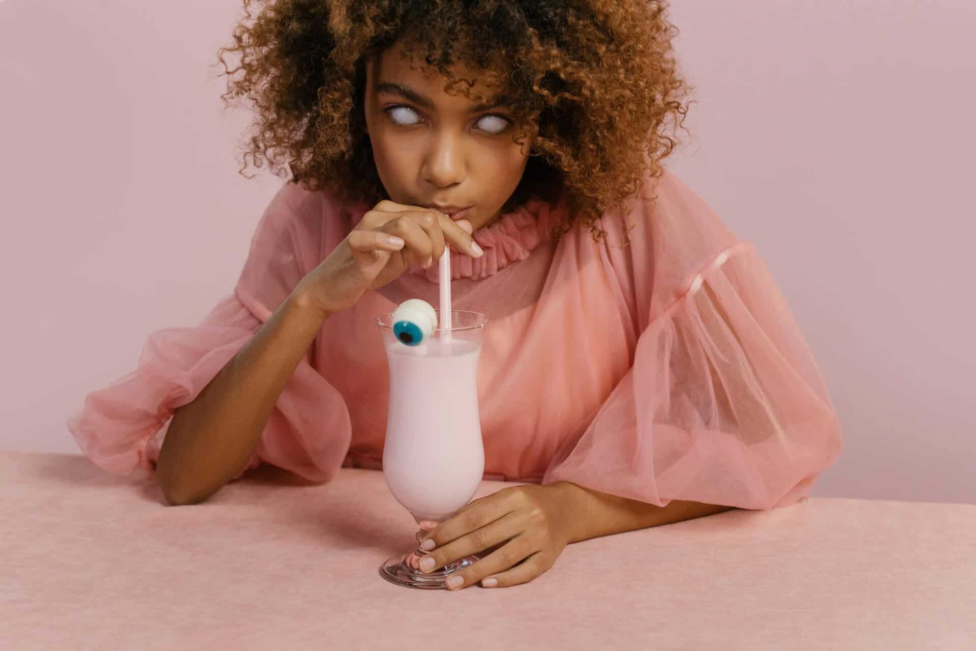 Young woman in a creative Halloween costume sipping a milkshake with a candy eyeball. halloween drinks