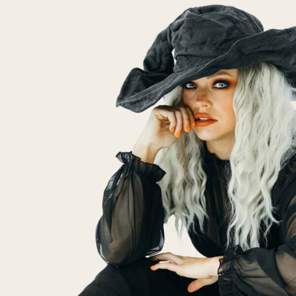 This photograph features a woman in orange Halloween makeup and a witch costume. Witchy glam is a versatile Halloween look.
