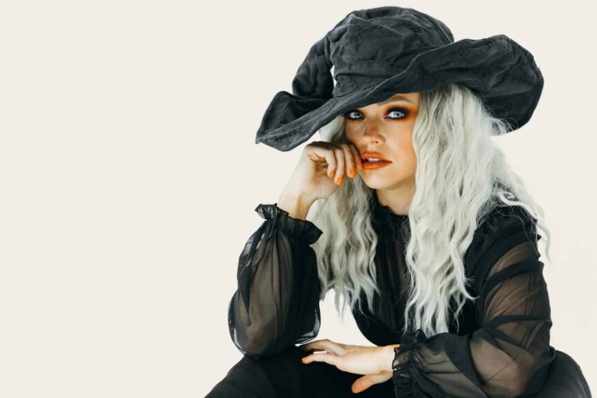 This photograph features a woman in orange Halloween makeup and a witch costume. Witchy glam is a versatile Halloween look.