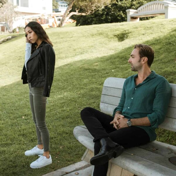 A couple having a disagreement on a park bench in a grassy outdoor setting. gaslighting