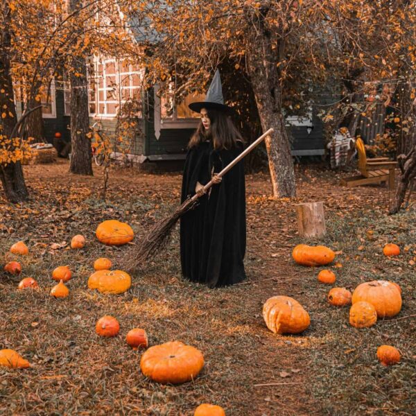 A witch in a classic costume stands among pumpkins in a fall-themed backyard, creating a perfect Halloween vibe of pure Autumn magic.