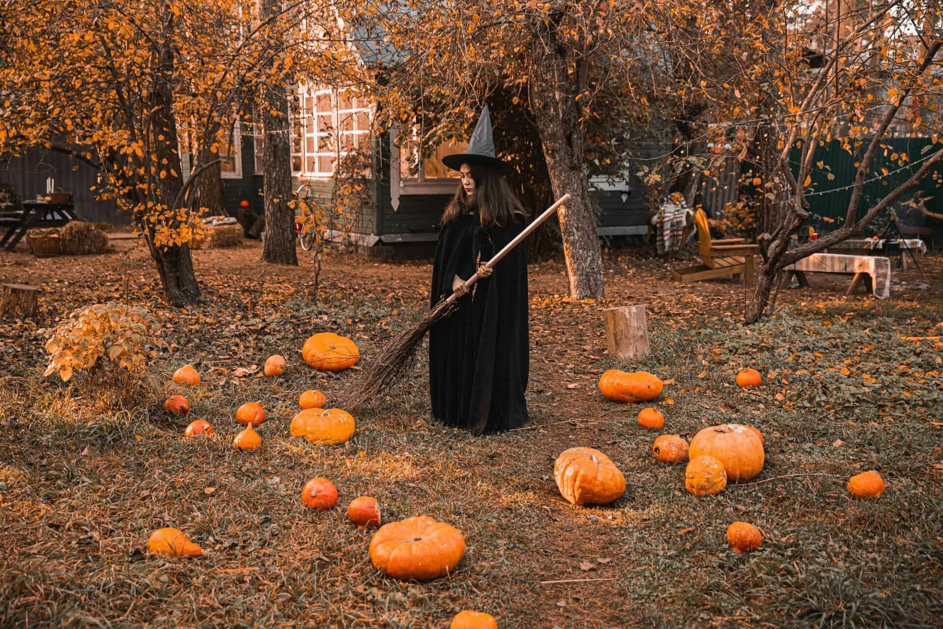 A witch in a classic costume stands among pumpkins in a fall-themed backyard, creating a perfect Halloween vibe of pure Autumn magic.