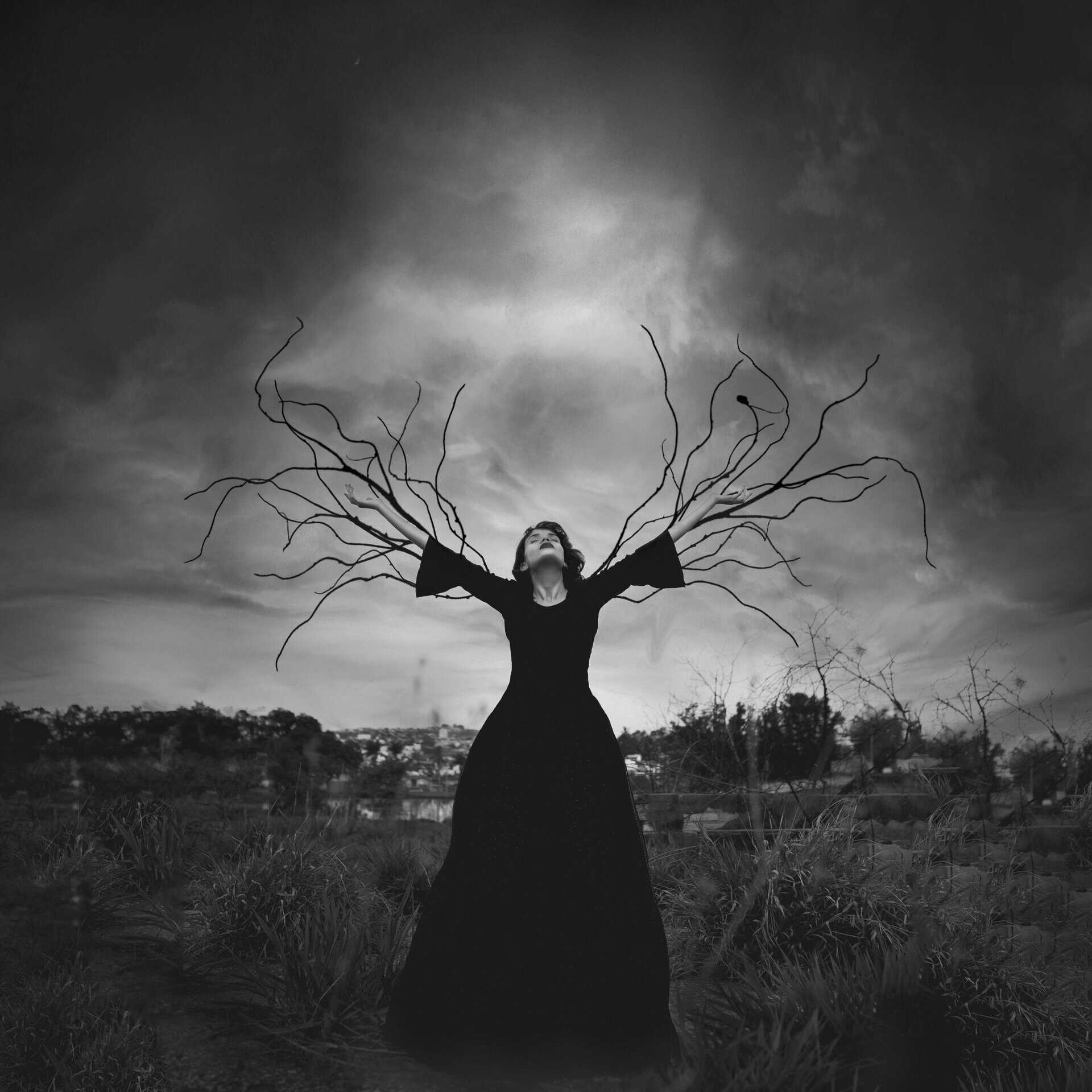 A captivating black and white image of a woman with branch-like arms reaching toward the sky, creating a mystical atmosphere. Capricorn energy. 