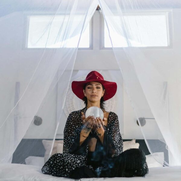 A woman wearing a red hat holds a crystal ball in an ethereal setting, suggesting mystery and magic. Intuitive list of zodiac signs.