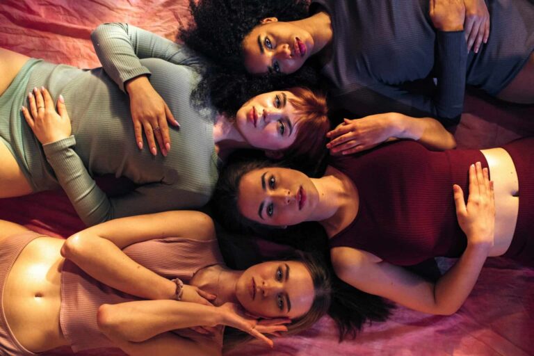 Empowered diverse women lying on pink fabric, showing unity and beauty. Women's Health and Depression.