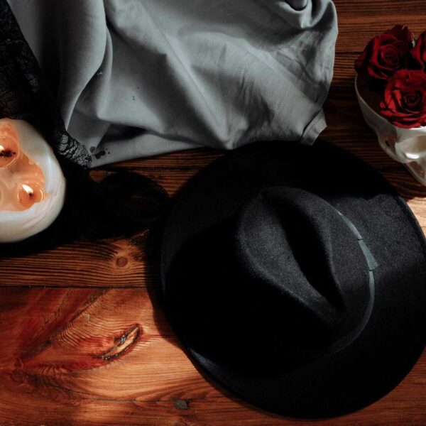 Flat lay image with black hat, skull, candles, and roses on wooden surface. Shadow work by zodiac sign.