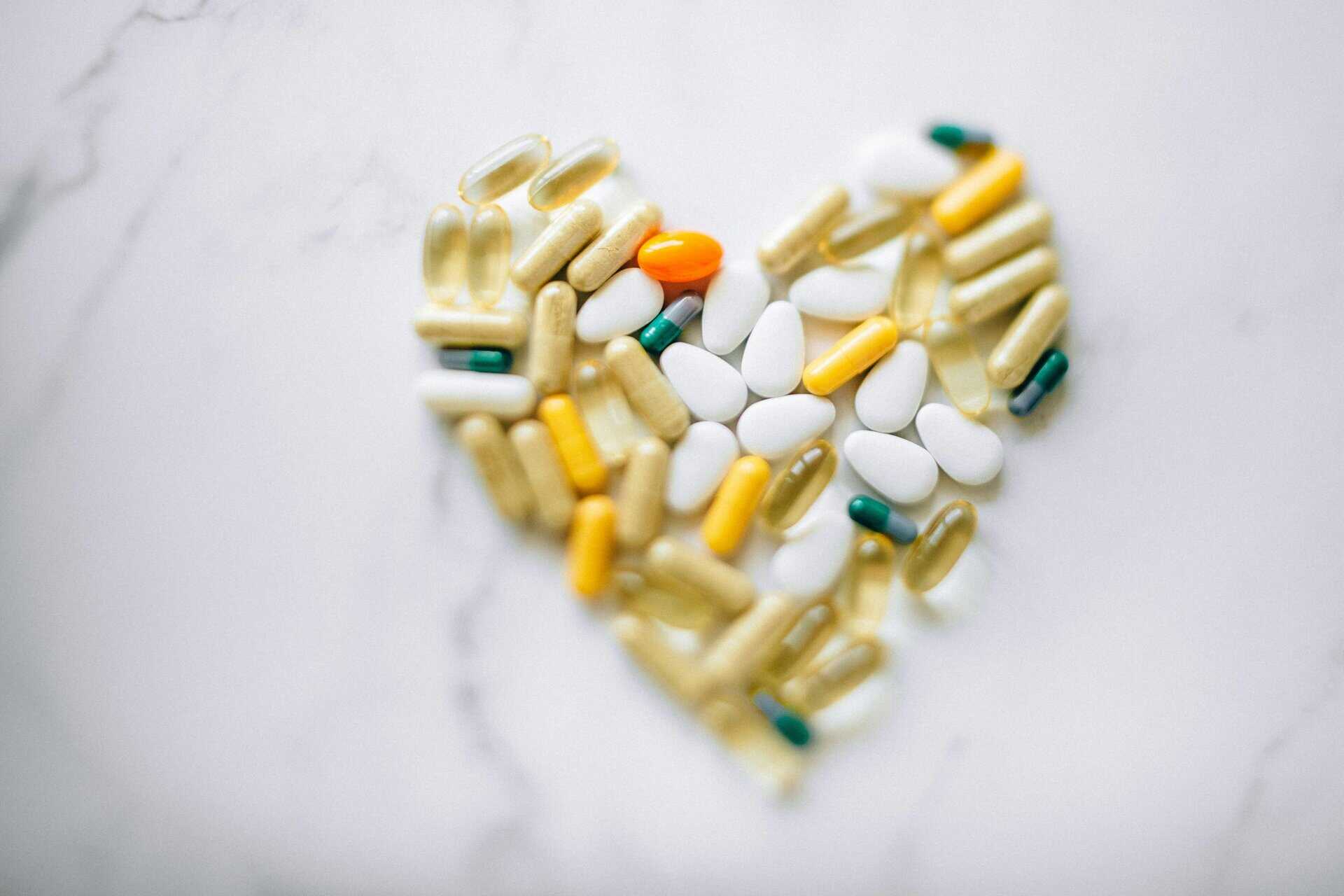 Colorful pills arranged in heart shape on a marble surface, symbolizing health and wellness, anti-aging.