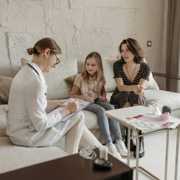 A doctor consults with a mother and daughter in a cozy indoor setting, children's emotional wellness
