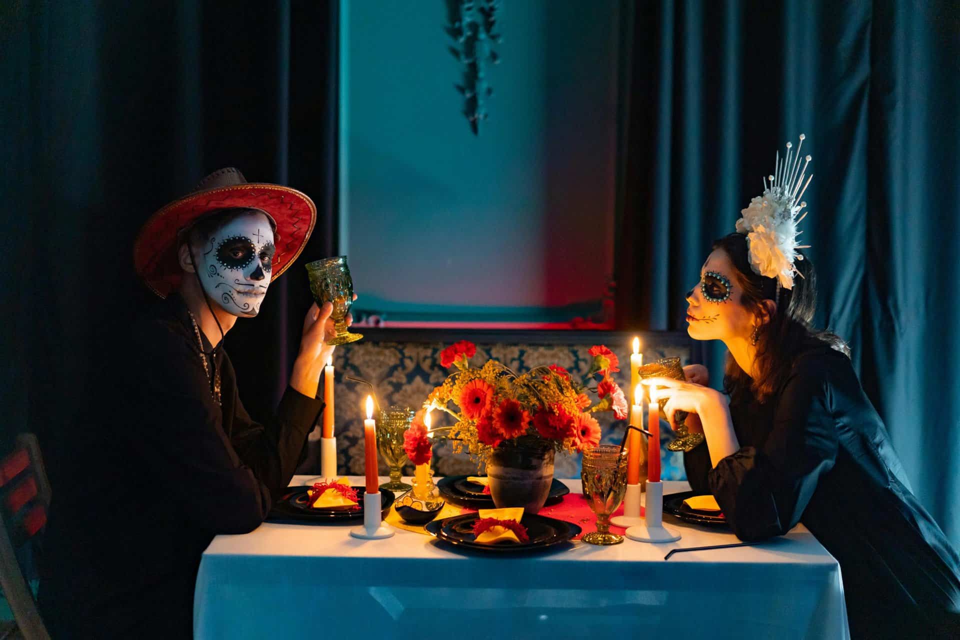 Couple celebrating Day of the Dead with face paint and candlelit dinner in colorful decor.