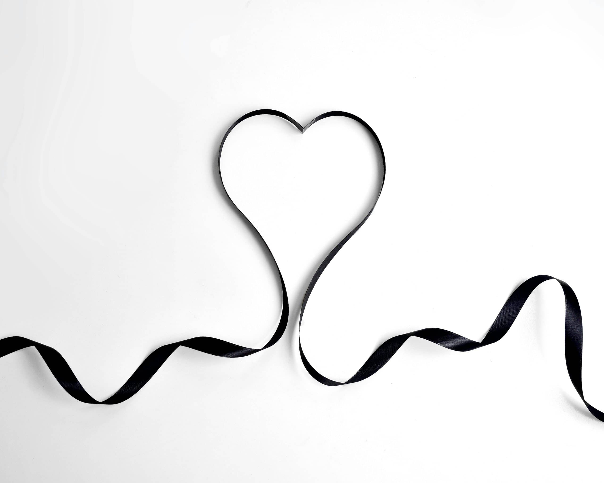 Black ribbon shaped like a heart on a white background, symbolizing love or romance.