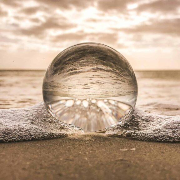 A crystal ball resting on Bonita Springs beach reflecting ocean waves at sunset. Aquarius inspirations.