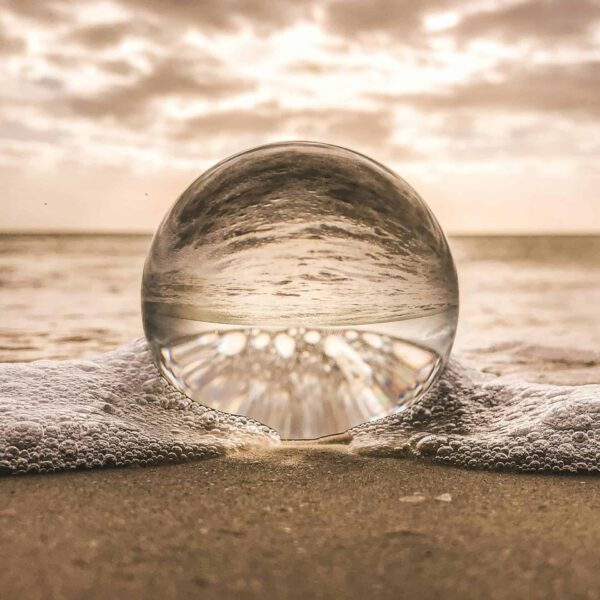 A crystal ball resting on Bonita Springs beach reflecting ocean waves at sunset. Aquarius inspirations.