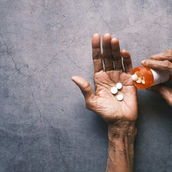 Elderly person's hand pouring pills from a bottle, offering ample copy space, slower aging.