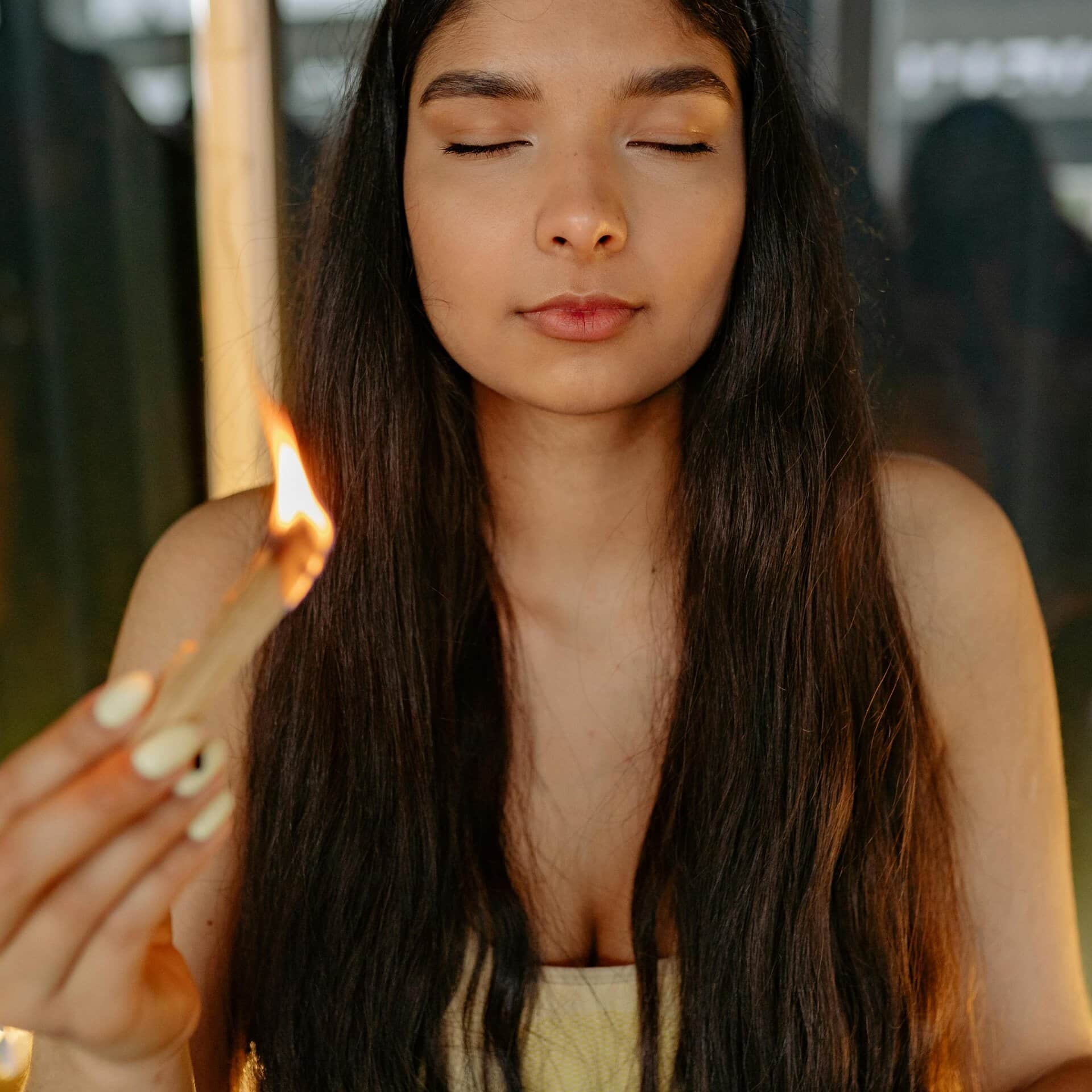 A serene woman meditating indoors, holding a burning incense stick with eyes closed, practicing mindfulness. Reflecting on their Aquarian forecast. 